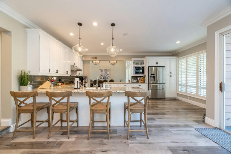 Spacious and immaculate kitchen with modern design. The room is well-lit by stylish pendant lights hanging over a large island with a polished marble countertop. Read our blog for more renovation tips.